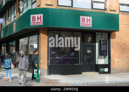 New York, NY, USA - 21. März 2024: Grünes und braunes Gebäude des B H-Geschäfts unter klarem Himmel, Fußgänger passieren eine Kreuzung. Stockfoto