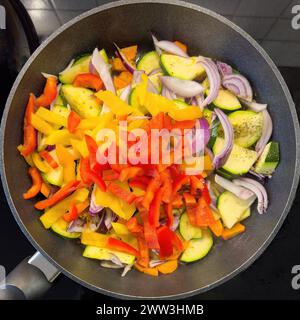 Vegetarisches veganes Gericht Gemüsepfanne mit Zucchini rote gelbe Paprika Zwiebeln Gemüsezwiebeln Karotten Gemüse wird mit Olivenöl gebraten Stockfoto