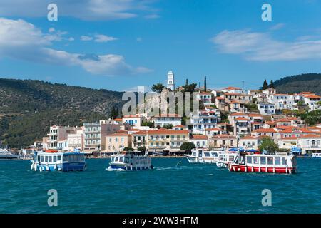Blick auf einen lebhaften Hafen mit bunten Häusern vor einem Hügel unter blauem Himmel mit Wolken, Wassertaxi, Blick von Galatas, Argolis, nach Poros Stockfoto