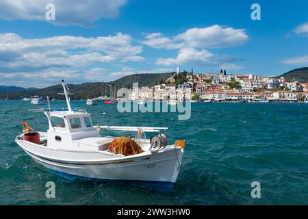 Ein Fischerboot auf dem Meer vor einer malerischen Küstenstadt unter einem teilweise bewölkten blauen Himmel, Blick von Galatas, Argolis, nach Poros, Poros Insel Stockfoto