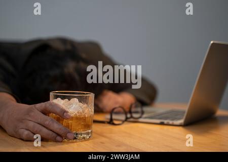 Ein sehr müder oder gestresster Geschäftsmann hält Whiskey und Drink in einem Business-Arbeitsplatz. Stockfoto
