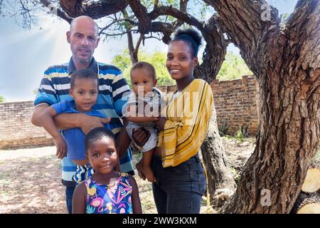 afrikanische Familie mit drei Kindern, die im Hinterhof stehen, in der Gemeinde, am späten Nachmittag, Stockfoto