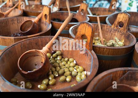 Nahaufnahme grüner Oliven in Holzschüsseln mit Schaufeln an einem Marktstand Stockfoto