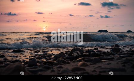 Rosafarbener Sonnenuntergang mit Wellen, die auf einen Kieselstrand stürzen Stockfoto