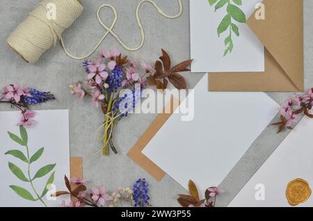 Weißes Papier mit Platz zum Einfüllen von Inhalt, kleinen blauen und rosa Blumen und Umschlägen auf einem Tisch. Stockfoto