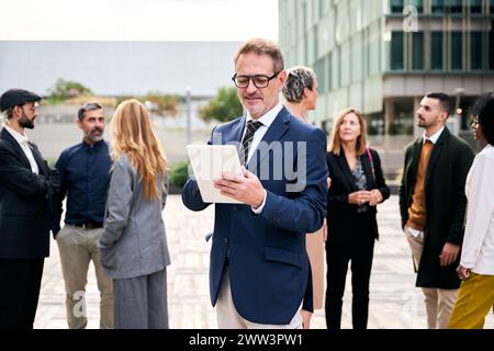 Ein kaukasischer Arbeiter mittleren Alters in formeller Kleidung, der vor einer Menschenmenge steht Stockfoto