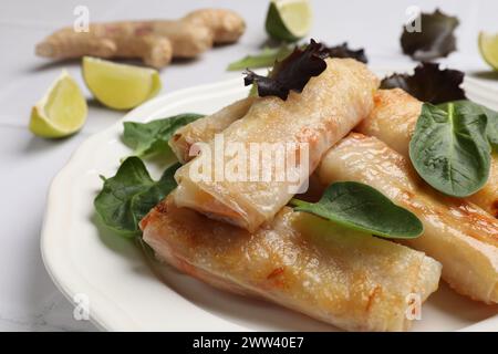 Teller mit leckeren gebratenen Frühlingsrollen und Spinat auf weißem Tisch, Nahaufnahme Stockfoto