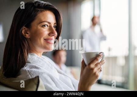 Junge ruhige entspannte Frau im Spa, die heißes Getränk Tee Kaffee trinkt. Schönheitsbehandlung Hydratationskonzept Stockfoto