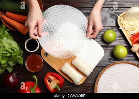 Köstliche Frühlingsbrötchen machen. Frau mit frischem Reispapier am Holztisch, flacher Lay Stockfoto