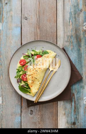 Omelette mit Kräutern, Fetakäse und Kirschtomaten auf einem Teller auf hellem Hintergrund, Blick von oben Stockfoto