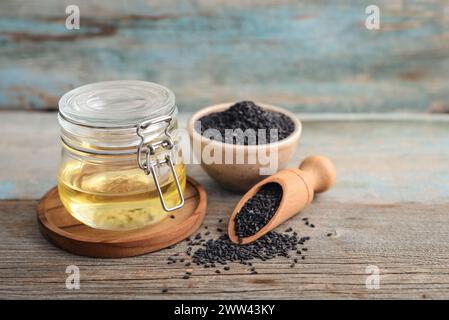 Schwarze Sesamsamen in Schüssel und Öl in Glasgefäß auf hölzernem Hintergrund Nahaufnahme. Stockfoto