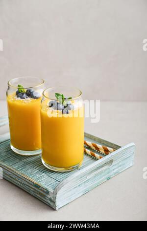 Erfrischender und gesunder Mango-Smoothie mit Kokosflocken und frischen Heidelbeeren auf hellem Hintergrund Stockfoto