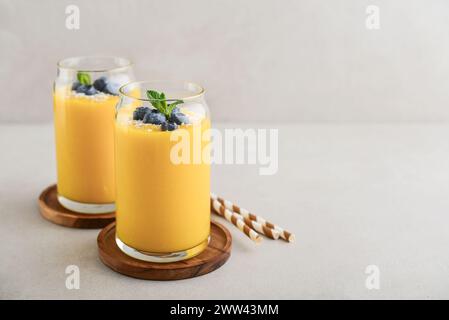 Erfrischender und gesunder Mango-Smoothie mit Kokosflocken und frischen Heidelbeeren auf hellem Hintergrund Stockfoto