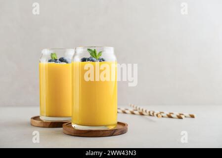 Erfrischender und gesunder Mango-Smoothie mit Kokosflocken und frischen Heidelbeeren auf hellem Hintergrund Stockfoto