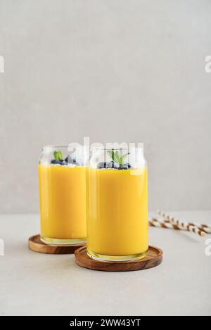 Erfrischender und gesunder Mango-Smoothie mit Kokosflocken und frischen Heidelbeeren auf hellem Hintergrund Stockfoto