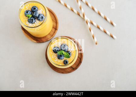 Erfrischender und gesunder Mango-Smoothie mit Kokosflocken und frischen Heidelbeeren auf hellem Hintergrund Stockfoto