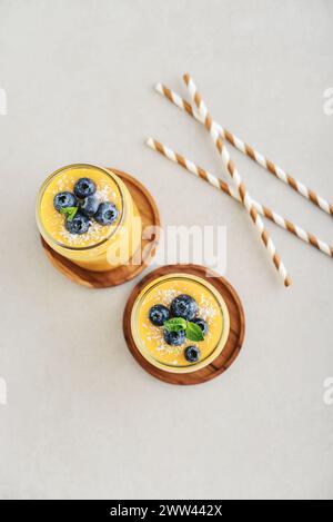 Erfrischender und gesunder Mango-Smoothie mit Kokosflocken und frischen Heidelbeeren auf hellem Hintergrund Stockfoto