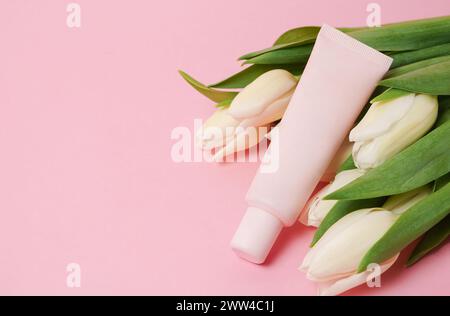 Beige Kosmetikröhre mit Creme oder Lotion für Körper und Bouquet von weißen Tulpen auf beigem Hintergrund Stockfoto