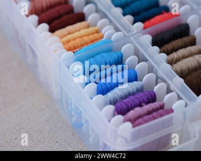Eine Nahaufnahme einer Plastiksortierbox voller Spulen mit verschiedenfarbigen Stickfäden auf beigefarbenem Leinwandhintergrund. Stockfoto