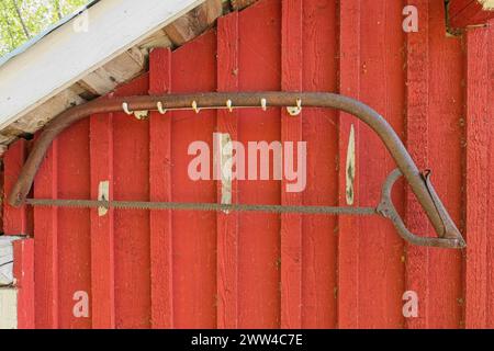 Nahaufnahme einer alten, rostigen Bogensäge (Schweißsäge, finn-Säge oder Bucksäge), die an einer Holzwand eines traditionell rot gestrichenen Gebäudes hängt. Stockfoto