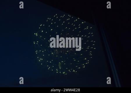 Kugelförmiges großes Feuerwerk am Nachthimmel, vom Fenster aus fotografiert Stockfoto