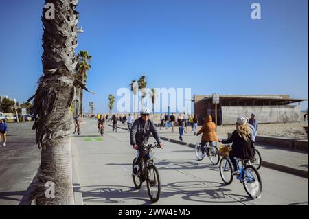 10. März 2024, Los Angeles, USA. Venedig Strand an einem hellen, sonnigen Tag. Menschenmassen Touristen Wanderweg entlang der Fußgängerzone des Broadwalk. Radfahrer fahren auf der Fahrradstraße. Wunderschöner Blick aufs Meer Stockfoto