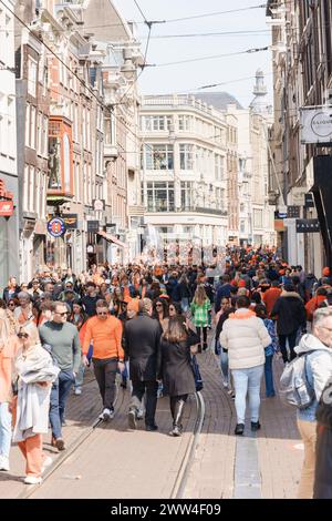 Viele Leute drängen sich in Orange auf der Straße. Es ist Königstag in Amsterdam, mit lustigen und alten Gebäuden - Niederlande, Amsterdam, 27.04.2023 Stockfoto