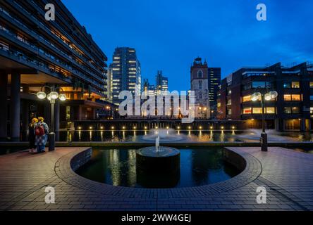 London, Großbritannien: Kirche, künstlicher Teich, Brunnen und zwei Personen auf dem Barbican Estate in der City of London. Stockfoto