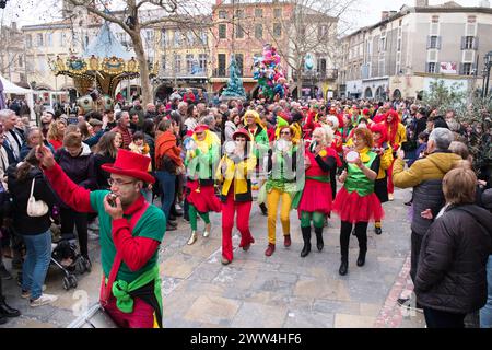 Limoux Aude France 03.02.24 Karnevalsparade. Bunt gekleidete Männer und Frauen mit Musikinstrumenten tanzen. Mittelalterlicher Marktplatz. Karussell, Statue Stockfoto