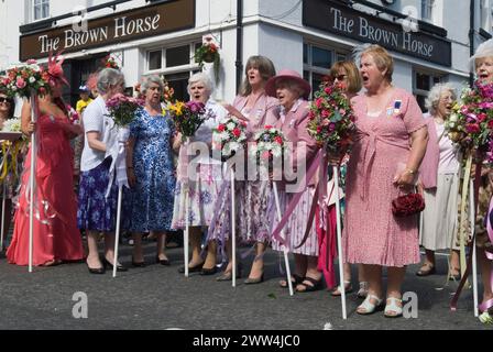 Neston Female Friendly Society Annual Club Walking Day. Ladies Club Mitglieder am Kreuz singen Hymnen und Land der Hoffnung und des Ruhms. Sie laufen mit Blumenstöcken. Neston, Cheshire, England, 4. Juni 2015. HOMER SYKES AUS DEN 2010ER JAHREN Stockfoto