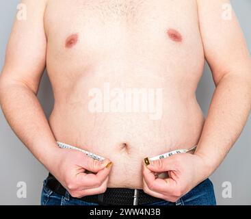 Nahaufnahme des übergewichtigen Bauches eines nicht erkennbaren kaukasischen Mannes mit einem Maßband, das nicht ausreicht, um seinen Bauch einzukreisen. Stockfoto