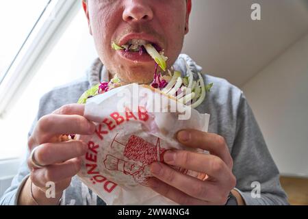 Augsburg, Bayern, Deutschland - 21. März 2024: Ein junger Mann beißt hungrig in einen vegetarischen Döner Döner mit viel Salat *** ein junger Mann beißt hungrig in einem vegetarischen Döner Kebap mit viel Salat Stockfoto