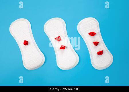 Damenhygienepads mit roten Blüten auf blauem Hintergrund. Erstes Menstruationskonzept, Menstruationszyklusperiode. Stockfoto