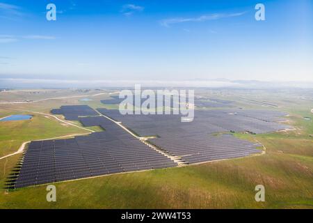 Ein großes Feld von Solarpaneelen ist über die Landschaft verteilt. Der Himmel ist klar und blau, und die Sonne scheint hell. Die Solarpaneele sind angeordnet Stockfoto