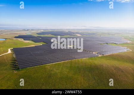 Ein großes Feld von Solarpaneelen ist über die Landschaft verteilt. Der Himmel ist klar und blau, und die Sonne scheint hell. Die Solarpaneele sind angeordnet Stockfoto