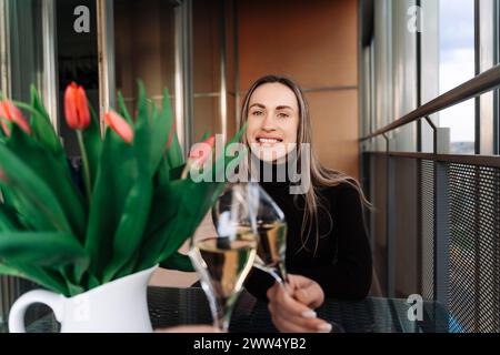 Junge Frau, die mit ihrem Freund beim Tisch sitzt, mit Blumenstrauß am Date Stockfoto