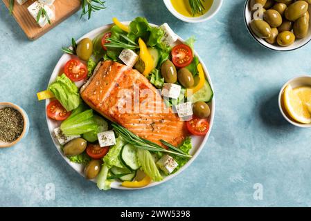 Gegrilltes Lachsfilet und frischer Gemüsesalat mit Fetakäse. Mediterrane Küche: griechischer Salat und gebratenes Lachssteak auf blauem Hintergrund. B Stockfoto