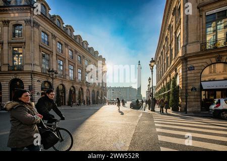 Die Rue de la Paix wird von Sonnenlicht überflutet, während Fußgänger überqueren, wobei der Place Vendôme in der Ferne sichtbar ist. Stockfoto