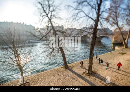 Fußgänger, die an einem sonnigen Wintertag entlang des seine-Ufers laufen, mit weichem Fokus durch ein neigbares Objektiv. Stockfoto