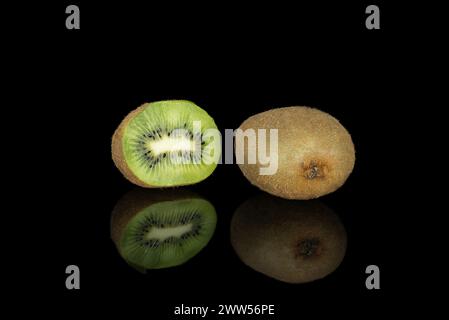 Zwei Kiwis isoliert auf schwarzem Hintergrund, einer davon in zwei Hälften. Stockfoto