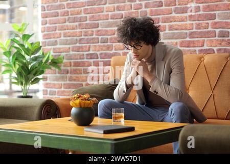 Junger Mann, der in einem Café sitzt und ein Glas Whiskey ansieht Stockfoto