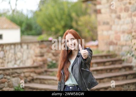 Eine junge Frau mit langen Haaren streckt ihre Hand aus und hebt ihren Daumen, um ihre Zustimmung zu geben Stockfoto