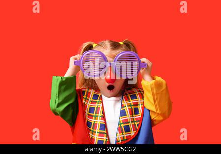 Lustiges Mädchen im Clown-Kostüm mit großer Brille auf rotem Hintergrund Stockfoto