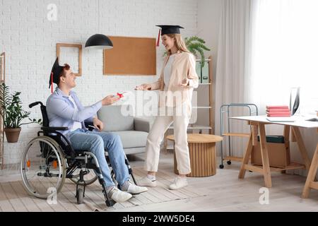 Männlicher Rollstuhlabsolvent mit Diplom und sein Klassenkamerad zu Hause Stockfoto