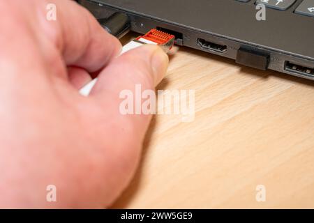 Stecken Sie einen hellgrauen Netzwerkstecker, der an ein CAT 7-Netzwerkkabel angeschlossen ist, von Hand in einen schwarzen Laptop. Stockfoto