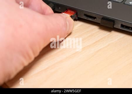 Stecken Sie einen hellgrauen Netzwerkstecker, der an ein CAT 7-Netzwerkkabel angeschlossen ist, von Hand in einen schwarzen Laptop. Stecker ist bereits im Steckplatz. Stockfoto