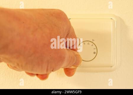Manuelle Änderung der Einstellung eines Drehknopfs zur Regulierung der Raumtemperatur an einem weißen Thermostat, der an einer Wand montiert ist. Stockfoto
