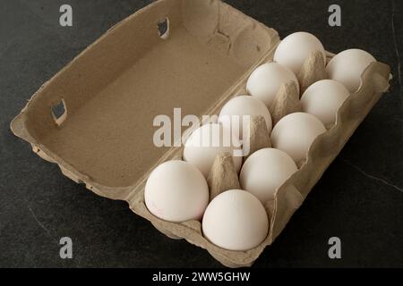 Braune offene Eierbox auf einem dunklen Tisch mit zehn weißen Eiern. Stockfoto