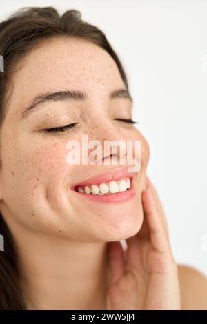 Glückliches, brünettes lateinamerikanisches Mädchen mit Sommersprossen, die das Gesicht auf weiß berühren. Vertikal Stockfoto
