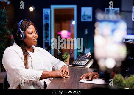 Während des Interviews nimmt eine schwarze Berühmtheit Inhalte für ihr Online-Publikum aus ihrem Heimstudio auf, indem sie ein Smartphone auf einem Stativ verwendet, während sie Fragen von einem Interviewer beantwortet. Stockfoto